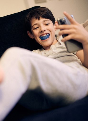 Young boy relaxing on couch, using myofunctional therapy appliance
