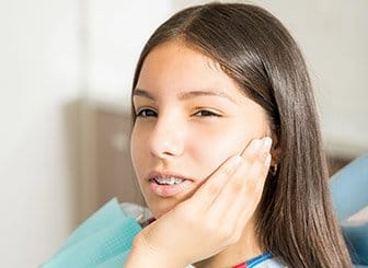 Teen girl with braces holding cheek in pain