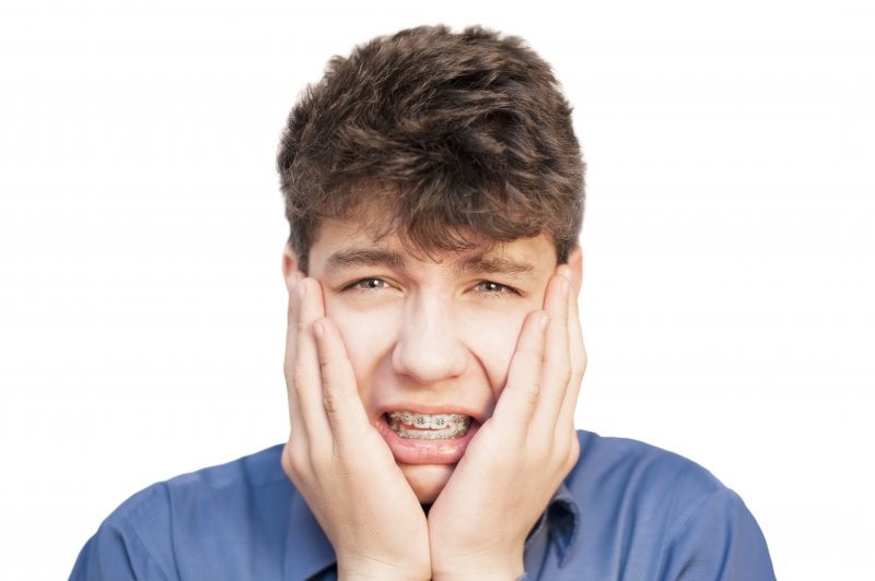 a young male teenager holding his face in pain while wearing metal braces