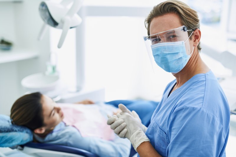 a dentist wearing personal protective equipment preparing to examine a female patient’s smile